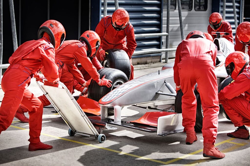 A team of pit crew members in red uniforms actively changing tires on a silver Formula One car, symbolizing teamwork and efficiency in website maintenance for the article section 'Key Components of Website Maintenance?' in 'Essential Monthly Website Maintenance Services for Small Businesses'.