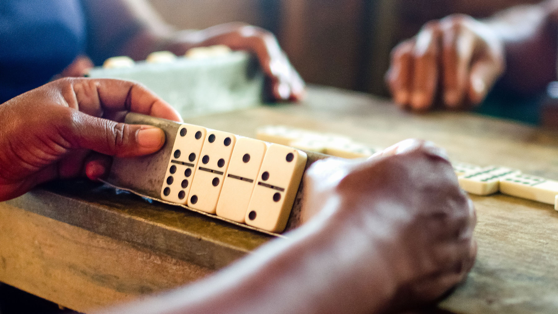 Close-up of hands playing a game of dominoes on a wooden table, illustrating the concept of the domino effect.